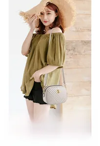 Detail of cream quilted camera bag with golden bee emblem and dual zipper design
