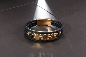 Macro detail of braided black leather bracelet featuring golden skull charms and magnetic clasp