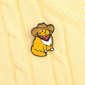 Close-up of a cute orange cowboy cat enamel pin accessorized on a yellow sweater