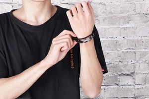 Detail of multi-layer black braided leather bracelet with silver wrench charm on male wrist
