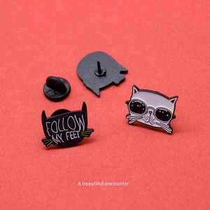 Detail of cartoon cat enamel pins showing front design and back rubber clutch attachment