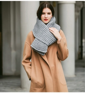 Detail of thick grey chunky knit scarf worn with a beige coat in an outdoor setting