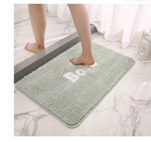 Detailed view of light green plush bath mat with BATH lettering on marble floor