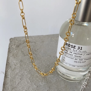 Detailed close-up of a minimalist gold geometric chain necklace on a textured grey surface