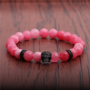 Macro detail of pink agate beads and black skull charm on a dark wooden surface