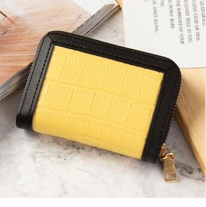 Detail of yellow crocodile pattern card holder with gold zipper on marble surface