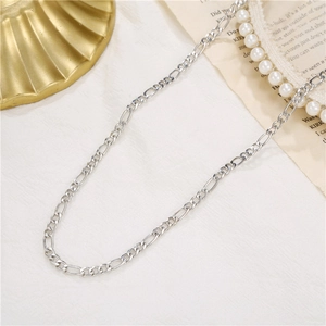 Detail shot of a silver Figaro chain necklace styled with elegant pearls on soft fabric