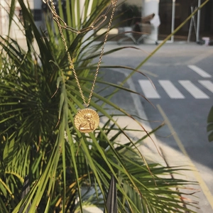 Close-up of double-layer golden necklace with Cupid angel relief pendant on palm leaf