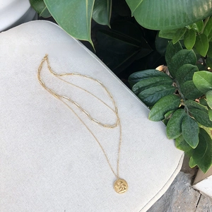 Close-up of gold layered chain necklace featuring a paperclip chain and cupid coin pendant