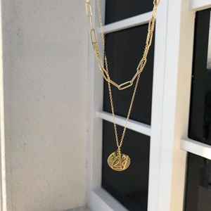 Close-up of golden double-layer paperclip chain necklace with a round cupid pendant
