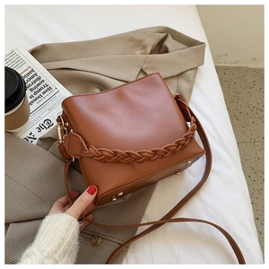 Detail of a brown PU leather bucket bag featuring a unique braided handle and metal feet