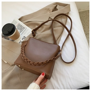 Detail of a brown leather bucket bag with woven handle and metal feet in office setting