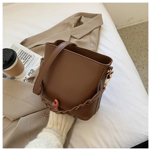 Brown PU leather bucket bag with braided handle styled on bed with a beige blazer