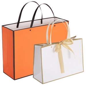 Orange and white paper gift bags with handles and ribbon bow for luxury shopping packaging