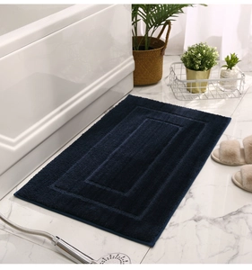 Dicke dunkelblaue saugfähige Badematte auf weißem Marmorboden neben einer Badewanne