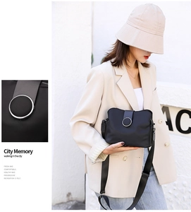 Detail of a black mini crossbody bag with a metal ring buckle and wide nylon strap