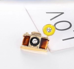 Macro detail of retro camera brooch with gold metal and colorful enamel finish