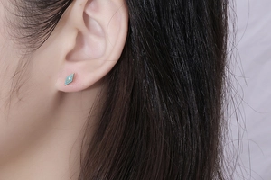 Close-up of light blue enamel rhombus stud earring with gold starburst on model's ear