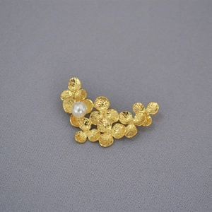 Detail of gold floral leaf brooch featuring matte petal texture and a white pearl accent