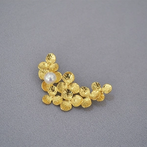 Detail of gold leaf brooch with hammered texture and round white pearl on grey fabric