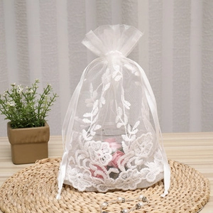 Detail of white organza drawstring bag with elegant lace floral embroidery and pink roses