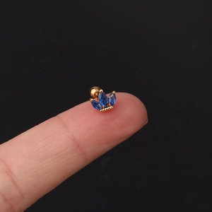 Macro shot of gold-plated crown stud with marquise blue zircon held on a fingertip