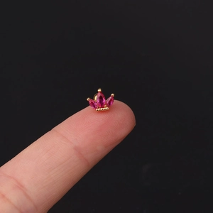 Macro shot of tiny gold crown earring with pink marquise stones held by fingers
