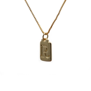 Close-up of a gold rectangle pendant necklace featuring an embossed letter R design