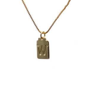 Detail of a golden rectangular pendant with an embossed letter W on a delicate box chain