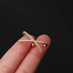 Crossed X-shape gold ear cuff with zircons held between fingers on black background
