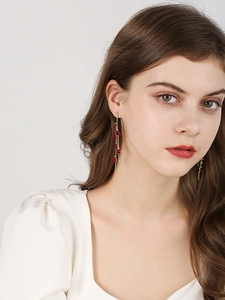 Détail de longues boucles d'oreilles dorées à pompons, fleurs rouges et cristaux