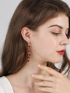 Gros plan de boucles d'oreilles à pompons avec roses rouges et chaînes dorées sur mannequin