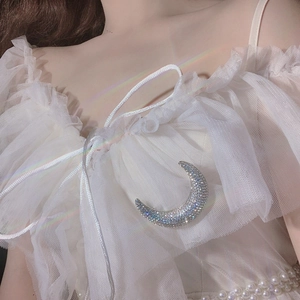 Macro detail of silver crescent moon brooch with sparkling rhinestones on model clothing