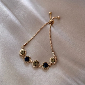 Adjustable gold plated bracelet with blue and green zircons on champagne satin background