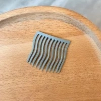 Minimalistischer grauer gewellter Haarkamm mit 10 Zähnen auf Holztablett präsentiert