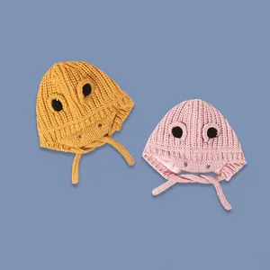 Cute dinosaur knitted baby hat with large eyes and chin straps in yellow and pink