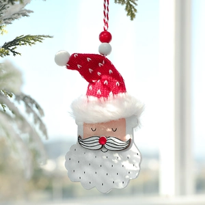Handcrafted wooden Santa Claus ornament with red knit hat hanging on a snowy pine branch