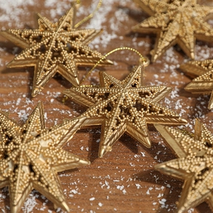 Golden star Christmas tree ornaments with fine textures on a snowy wooden background