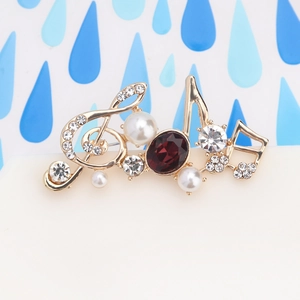 Macro shot of musical note brooch with red gemstone, pearls and crystals on gold plating