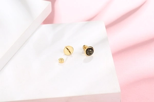 Detail of small gold circular stud earrings with black marble texture and screw-back closure