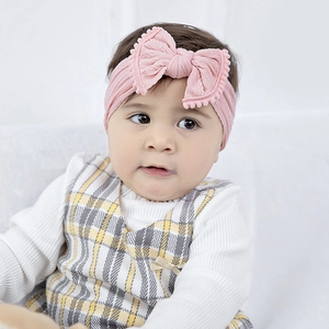 Close-up of baby pink ribbed headband with 3D bow and cute pom-pom edge detail