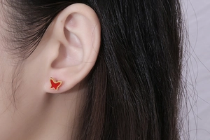 Close-up of elegant gold butterfly stud earring with vibrant red enamel on ear