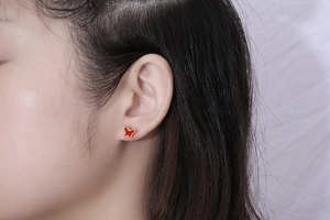 Close-up of a miniature red butterfly stud earring with a golden enamel edge on ear