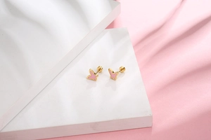 Macro shot of small butterfly stud earrings with pink enamel wings on marble surface