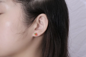 Close-up of a model wearing small red strawberry stud earrings with green leaf details