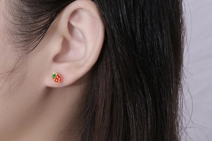 Close-up of cute red strawberry stud earrings on ear showing realistic size and detail