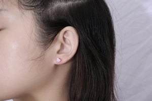 Close-up of heart-shaped earring in lavender enamel with gold edges worn by a model