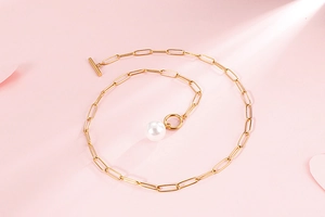 Detail of gold paperclip chain necklace with large white pearl and T-bar toggle clasp