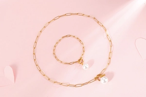 Detailed view of gold chain pearl necklace and bracelet set with OT clasp on pink background
