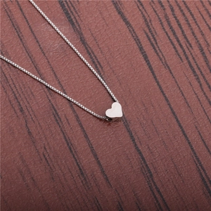 Macro shot of polished silver heart pendant on box chain over dark wood surface
